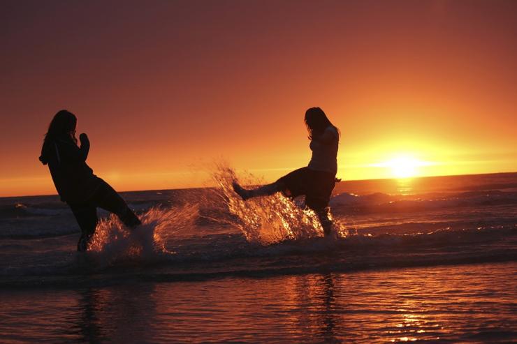 Deux personnes se jettent de l'eau à la figure sous un soleil couchant