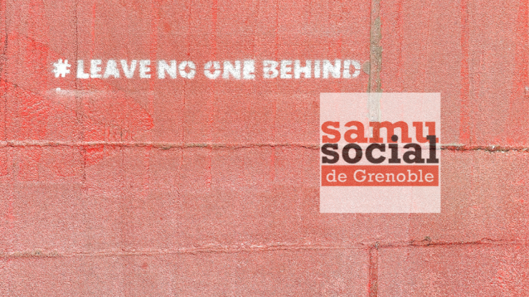 Mur en briques rouge avec une inscription blanche "leave no one behind" et le logo du samu social de Grenoble