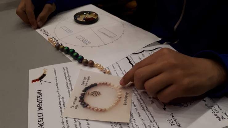 Tuto bracelet menstruel et mains en train de tenir un fil avec des perles de différentes couleurs.