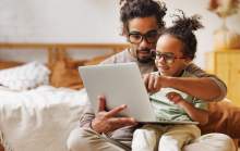 Parentalité numérique : un père utilisant son ordinateur portable avec son enfant sur les genoux.